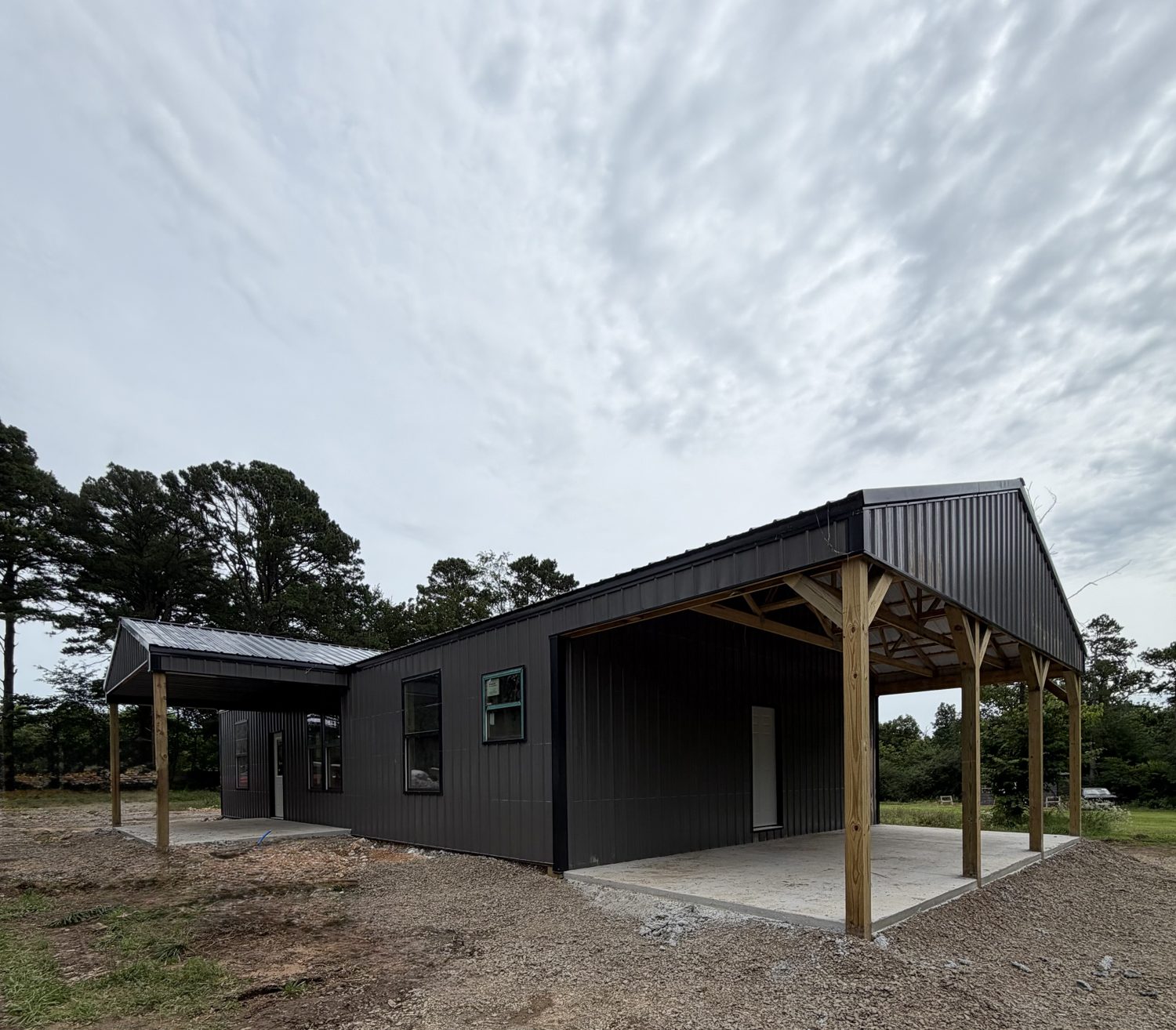 Black shop with an open roof extension over a concrete pad