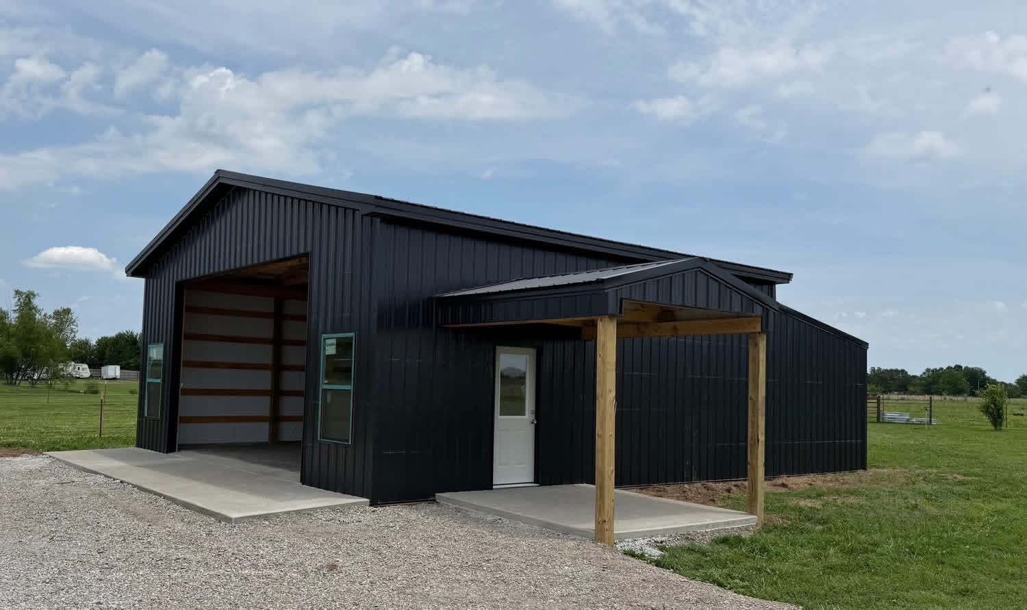 Black shop with a covered porch, white walk door, and concrete aprons