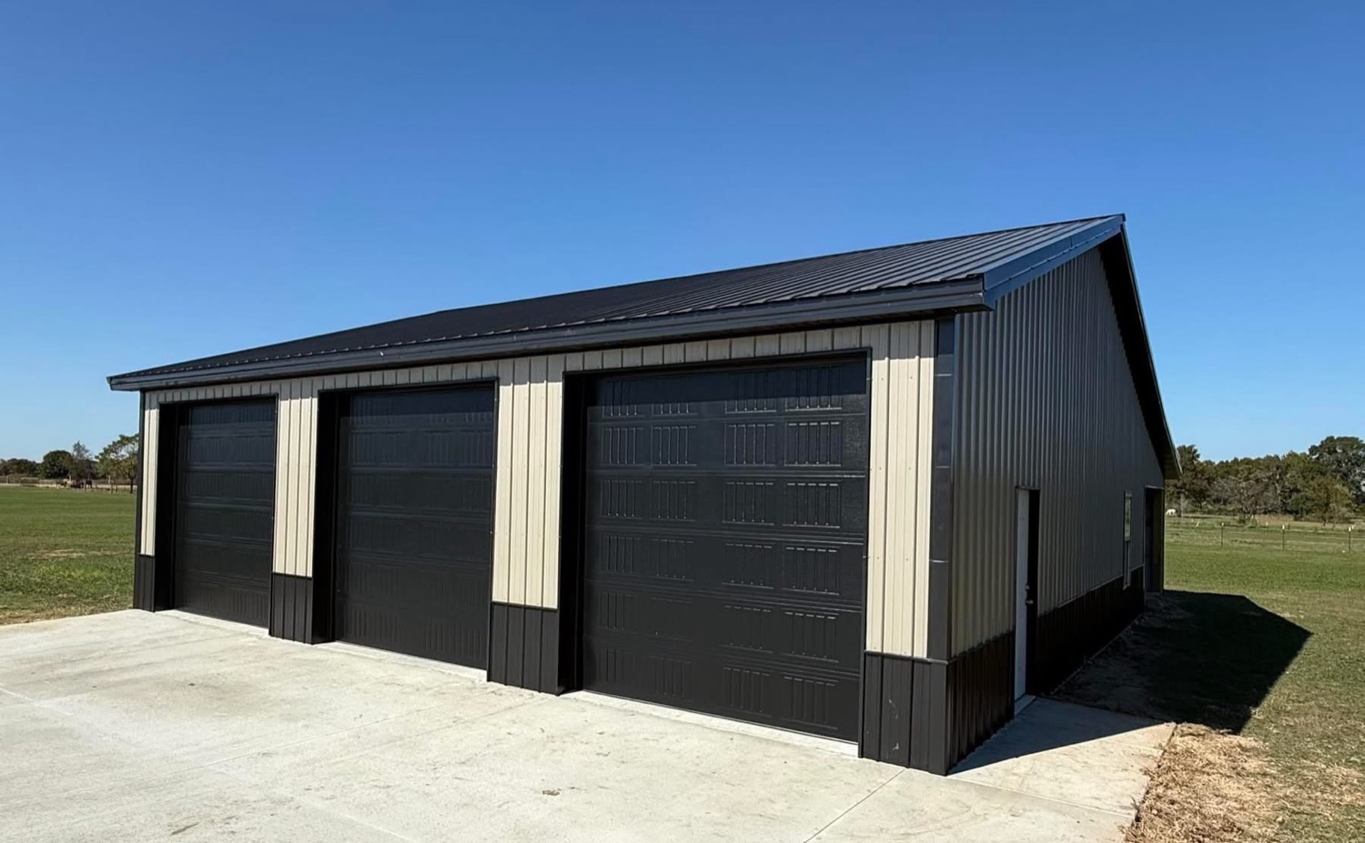 Three-bay shop with black insulated overhead doors, tan trim, and a black walk door